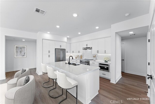 kitchen with sink, white cabinets, a kitchen bar, premium appliances, and a center island with sink