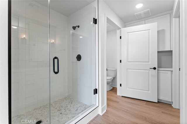 bathroom with hardwood / wood-style flooring, a shower with door, and toilet