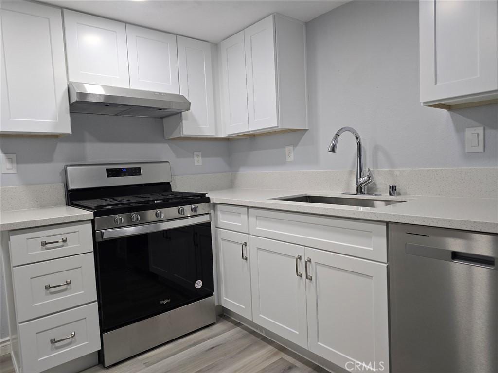 kitchen with white cabinets, sink, stainless steel appliances, and light hardwood / wood-style floors