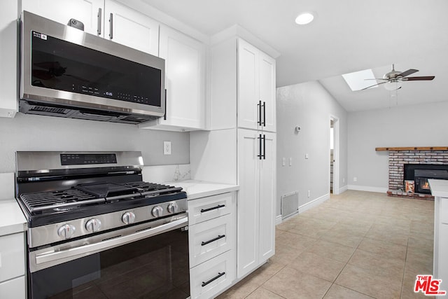 kitchen featuring appliances with stainless steel finishes, white cabinetry, a fireplace, light tile patterned flooring, and ceiling fan