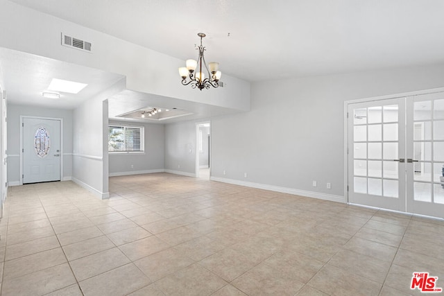 empty room featuring light tile patterned flooring, a chandelier, lofted ceiling, and french doors