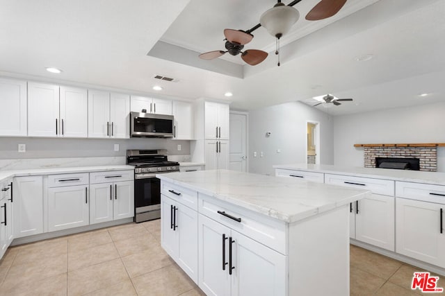 kitchen featuring a brick fireplace, stainless steel appliances, a raised ceiling, a kitchen island, and white cabinets