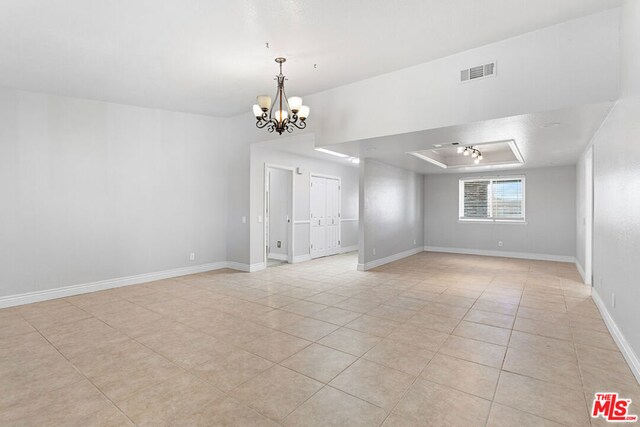 empty room with light tile patterned floors, a raised ceiling, and a notable chandelier