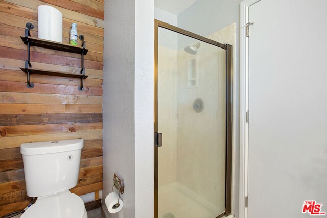 bathroom featuring toilet, a shower with door, and wood walls