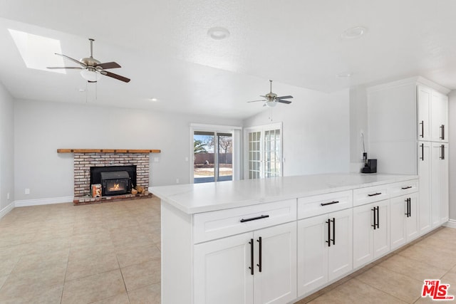 kitchen with kitchen peninsula, white cabinets, vaulted ceiling with skylight, and a brick fireplace