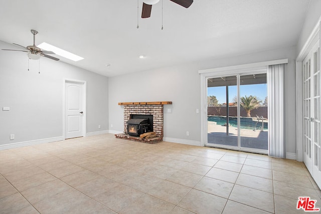 unfurnished living room with ceiling fan, light tile patterned floors, vaulted ceiling with skylight, and a wood stove