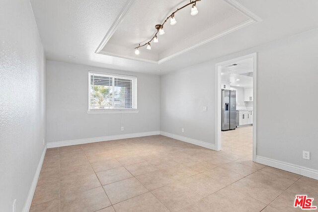 tiled empty room featuring crown molding, a tray ceiling, and a textured ceiling