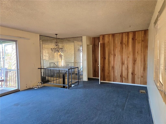 unfurnished room with an inviting chandelier, wooden walls, a textured ceiling, and dark carpet