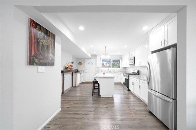 kitchen featuring pendant lighting, appliances with stainless steel finishes, a center island, white cabinetry, and a breakfast bar area