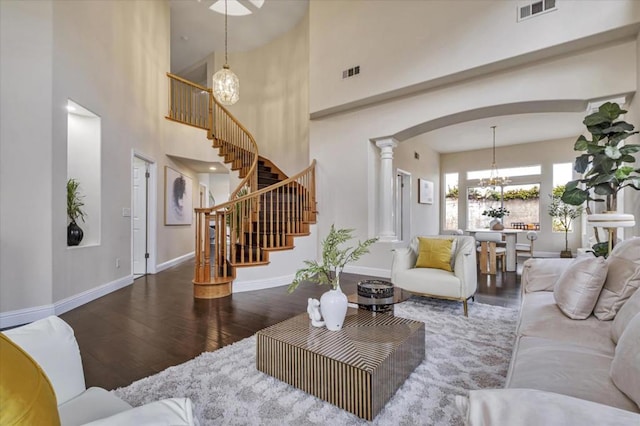 living room featuring a high ceiling, dark wood-type flooring, a chandelier, and decorative columns