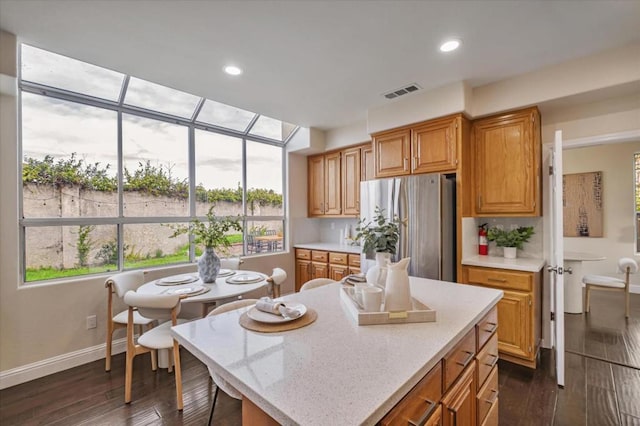 kitchen featuring a kitchen island, dark hardwood / wood-style flooring, stainless steel refrigerator, and light stone countertops