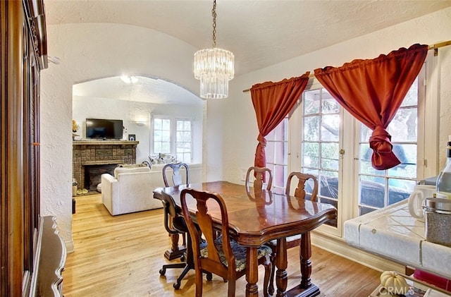 dining area with an inviting chandelier, lofted ceiling, a fireplace, and light hardwood / wood-style flooring