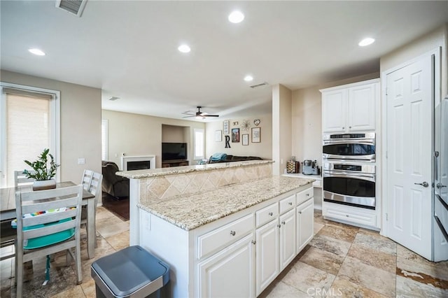 kitchen with ceiling fan, light stone counters, white cabinetry, and a kitchen island