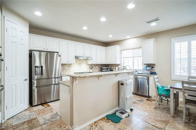 kitchen with a kitchen island, a breakfast bar, white cabinetry, appliances with stainless steel finishes, and light stone counters