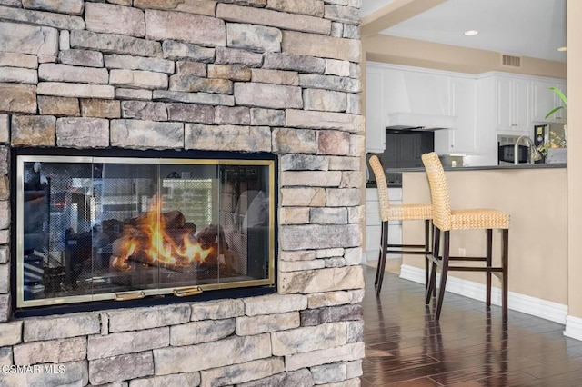 details with hardwood / wood-style flooring, custom range hood, and a stone fireplace