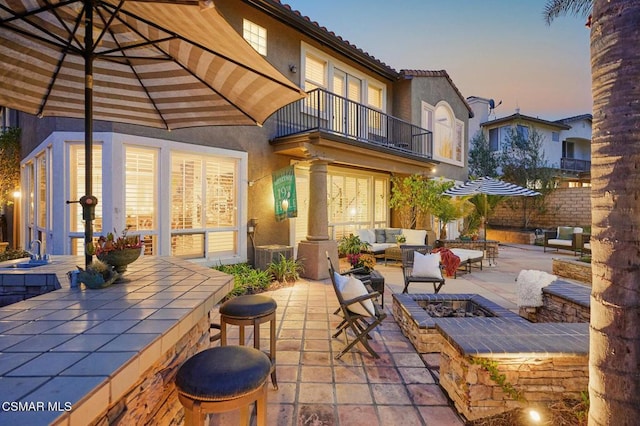 patio terrace at dusk featuring a balcony, an outdoor living space with a fire pit, and sink