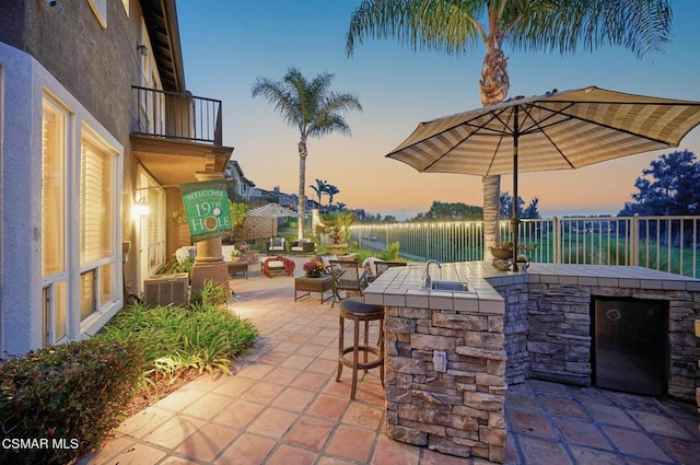 patio terrace at dusk featuring an outdoor wet bar and an outdoor kitchen