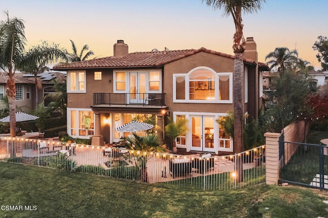 back house at dusk with a lawn and a balcony