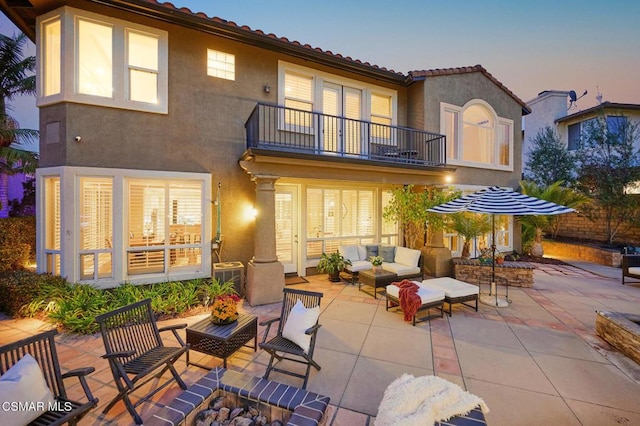 back house at dusk featuring a balcony, a patio area, and an outdoor living space