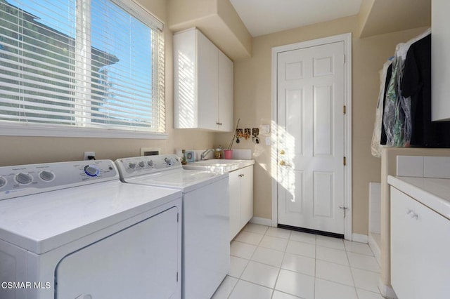 clothes washing area with washer and dryer, a wealth of natural light, light tile patterned floors, and cabinets