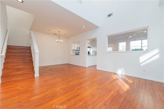 unfurnished living room featuring ceiling fan with notable chandelier and light hardwood / wood-style floors