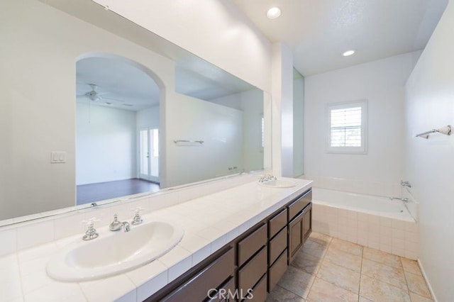 bathroom featuring ceiling fan, tiled tub, and vanity