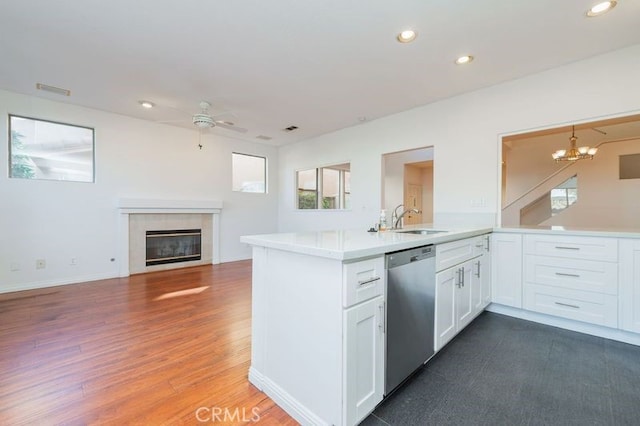 kitchen featuring white cabinetry, kitchen peninsula, stainless steel dishwasher, a tile fireplace, and sink