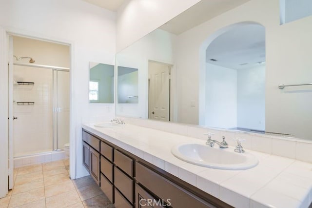 bathroom featuring a shower with shower door, toilet, vanity, and tile patterned flooring