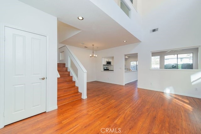 unfurnished living room featuring a towering ceiling, an inviting chandelier, and light hardwood / wood-style floors