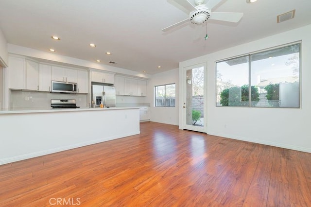 kitchen with ceiling fan, kitchen peninsula, white cabinetry, hardwood / wood-style flooring, and stainless steel appliances