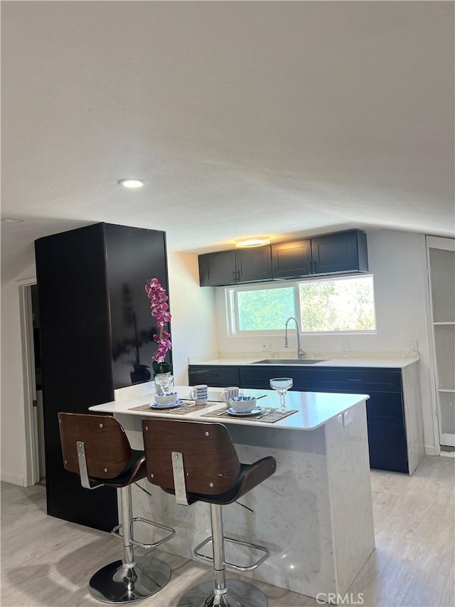 kitchen featuring light hardwood / wood-style floors, a kitchen bar, a center island, and sink