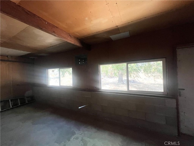 unfurnished room with beam ceiling, a healthy amount of sunlight, and concrete floors