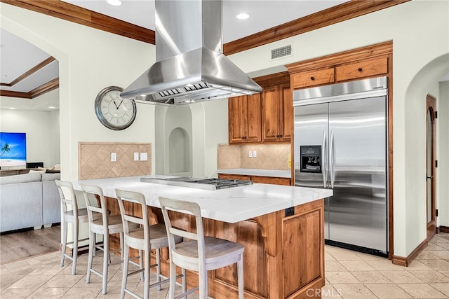 kitchen featuring backsplash, appliances with stainless steel finishes, island range hood, and ornamental molding