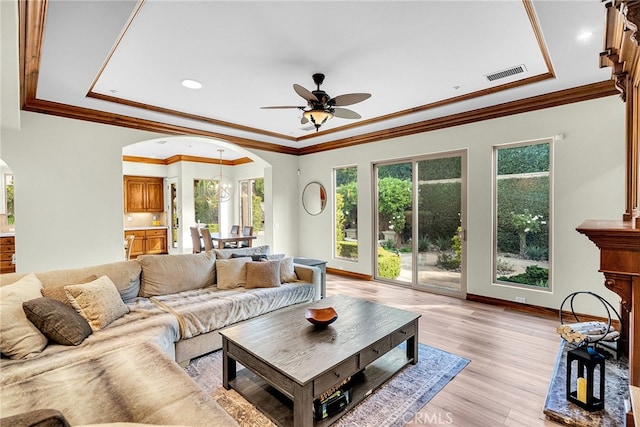 living room featuring a raised ceiling, light wood-type flooring, crown molding, and ceiling fan