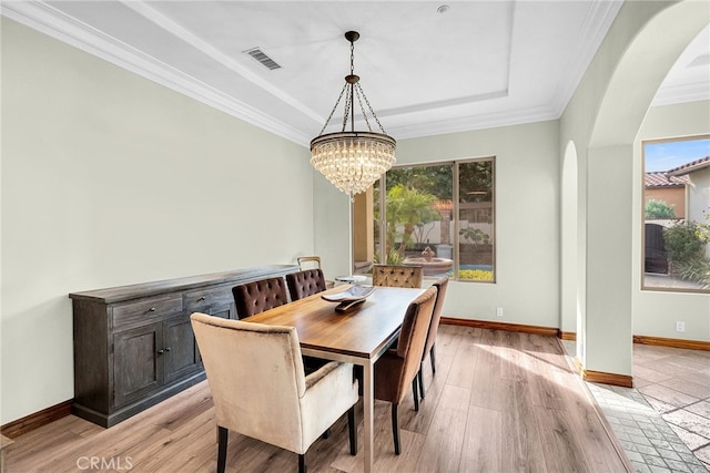 dining room featuring a raised ceiling, light wood-type flooring, a notable chandelier, and ornamental molding