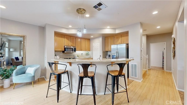 kitchen featuring appliances with stainless steel finishes, backsplash, light wood-type flooring, a kitchen breakfast bar, and a kitchen island