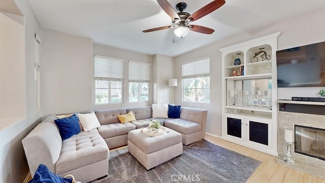 living area with a fireplace with flush hearth, ceiling fan, and wood finished floors