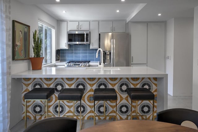 kitchen with backsplash, kitchen peninsula, sink, stainless steel appliances, and white cabinets