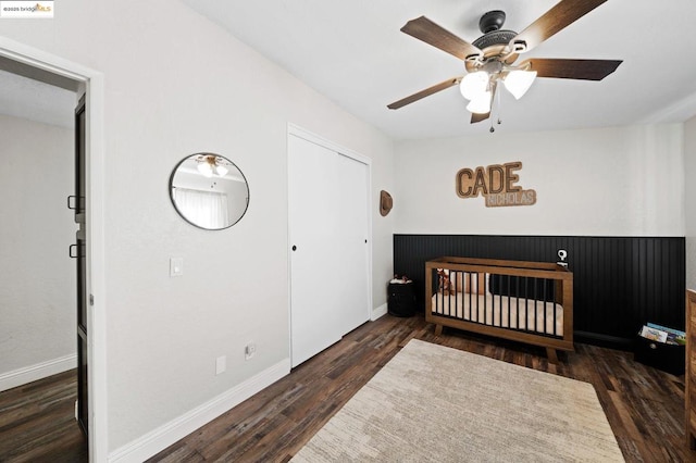 bedroom featuring a crib, ceiling fan, dark hardwood / wood-style flooring, and a closet