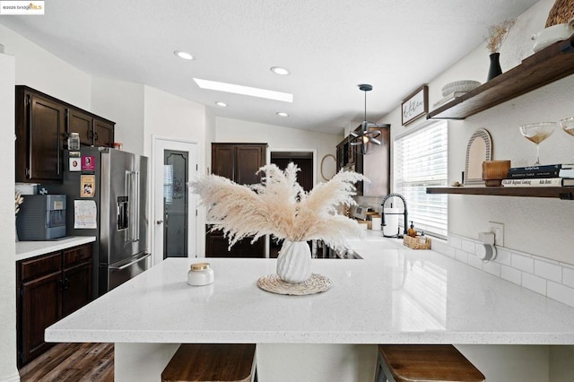 kitchen with dark brown cabinetry, a breakfast bar area, hanging light fixtures, high quality fridge, and vaulted ceiling with skylight