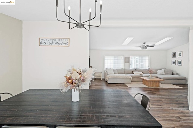 unfurnished dining area featuring dark wood-type flooring, a skylight, and ceiling fan with notable chandelier