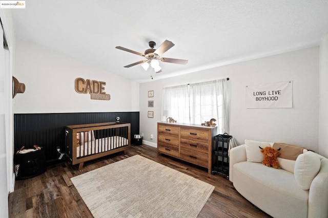 bedroom featuring a crib, dark hardwood / wood-style floors, and ceiling fan