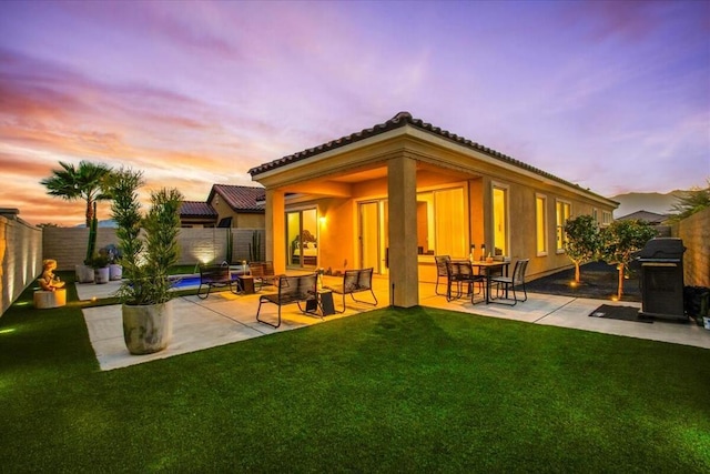 back house at dusk featuring a patio and a lawn