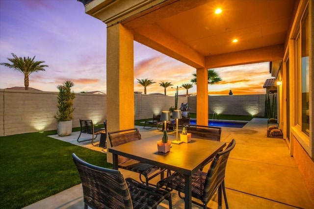 patio terrace at dusk featuring a water view and a lawn