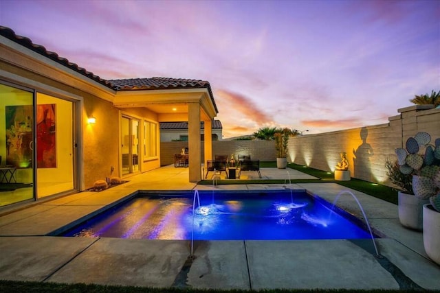 pool at dusk featuring a patio and pool water feature