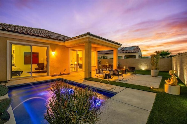 pool at dusk with pool water feature and a patio area