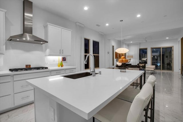 kitchen featuring sink, a kitchen breakfast bar, an island with sink, wall chimney range hood, and white cabinets