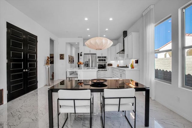 kitchen featuring wall chimney range hood, stainless steel appliances, white cabinets, and a kitchen bar