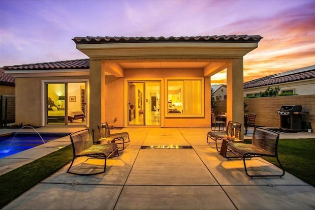 back house at dusk featuring a fenced in pool, a patio, and pool water feature