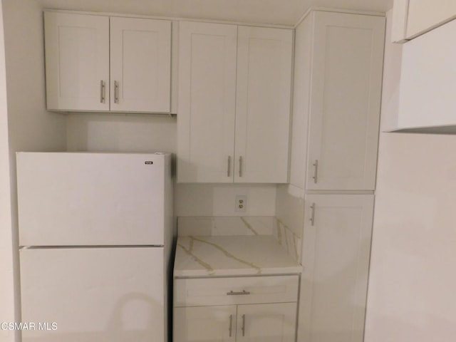 kitchen featuring white cabinets, light stone counters, and white fridge